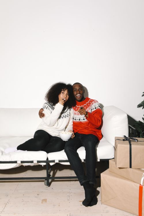 Free Smiling couple in festive sweaters enjoying Christmas time on a cozy sofa indoors. Stock Photo