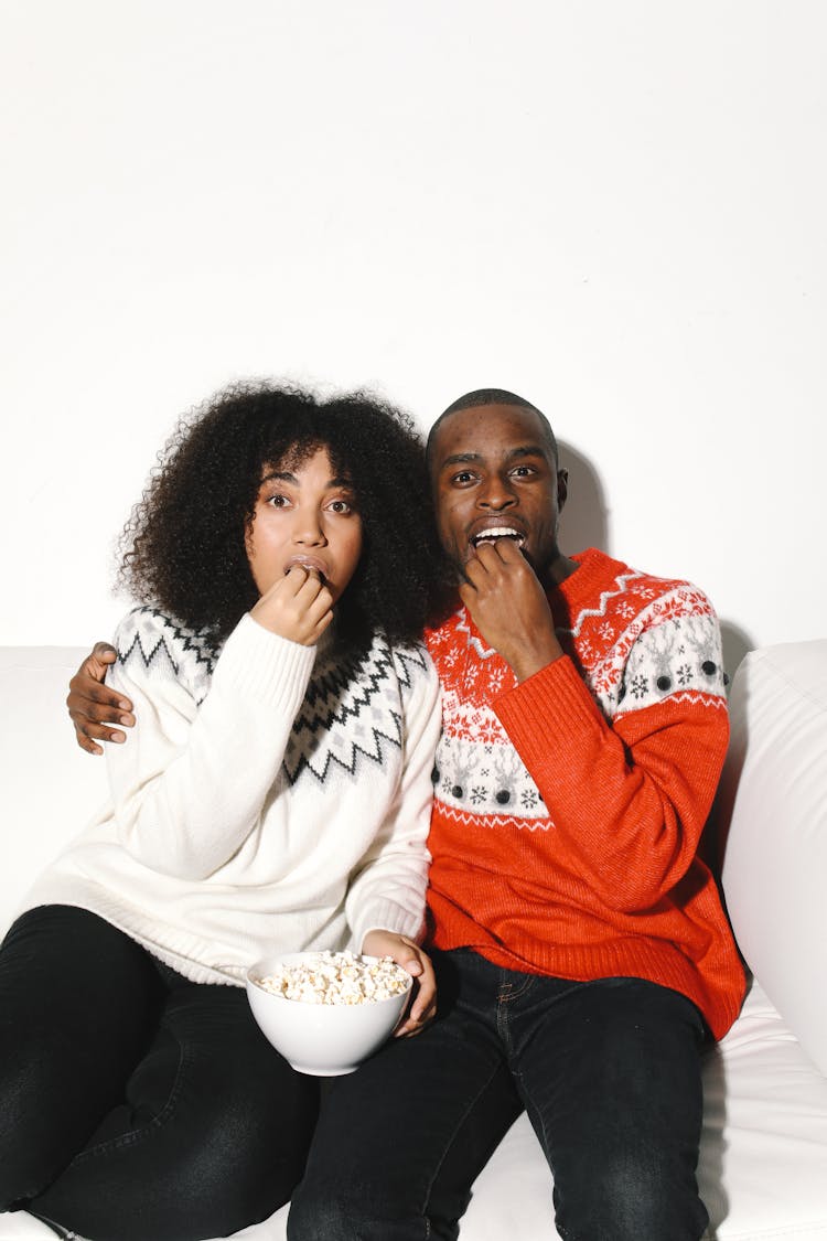 A Couple In Ugly Christmas Sweaters  Eating Popcorn In A Bowl