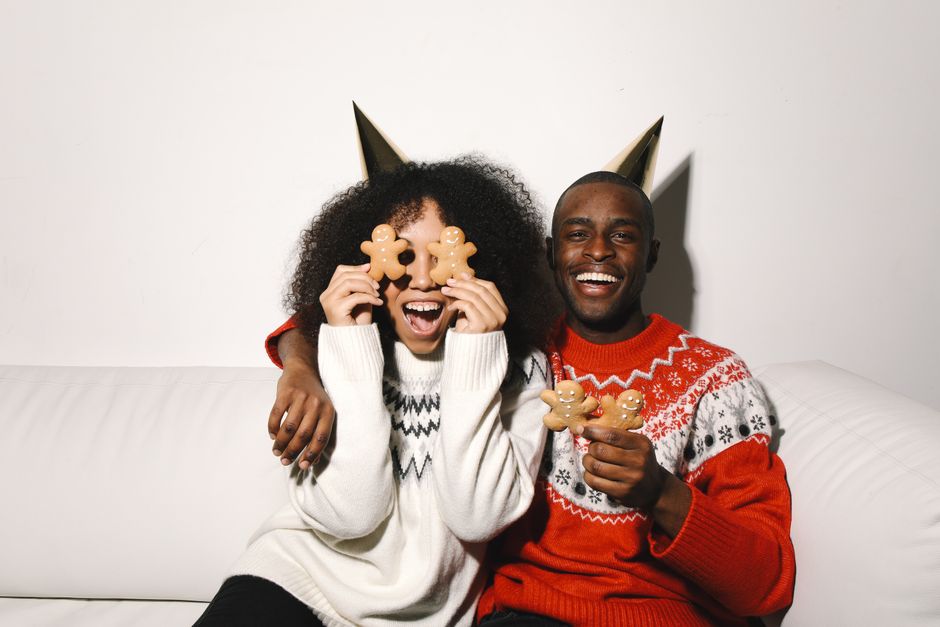 Joyful couple in Christmas sweaters celebrating with gingerbread cookies indoors.