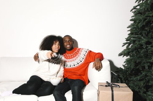 Free Young couple on a sofa enjoying the holiday season next to a Christmas tree. Stock Photo