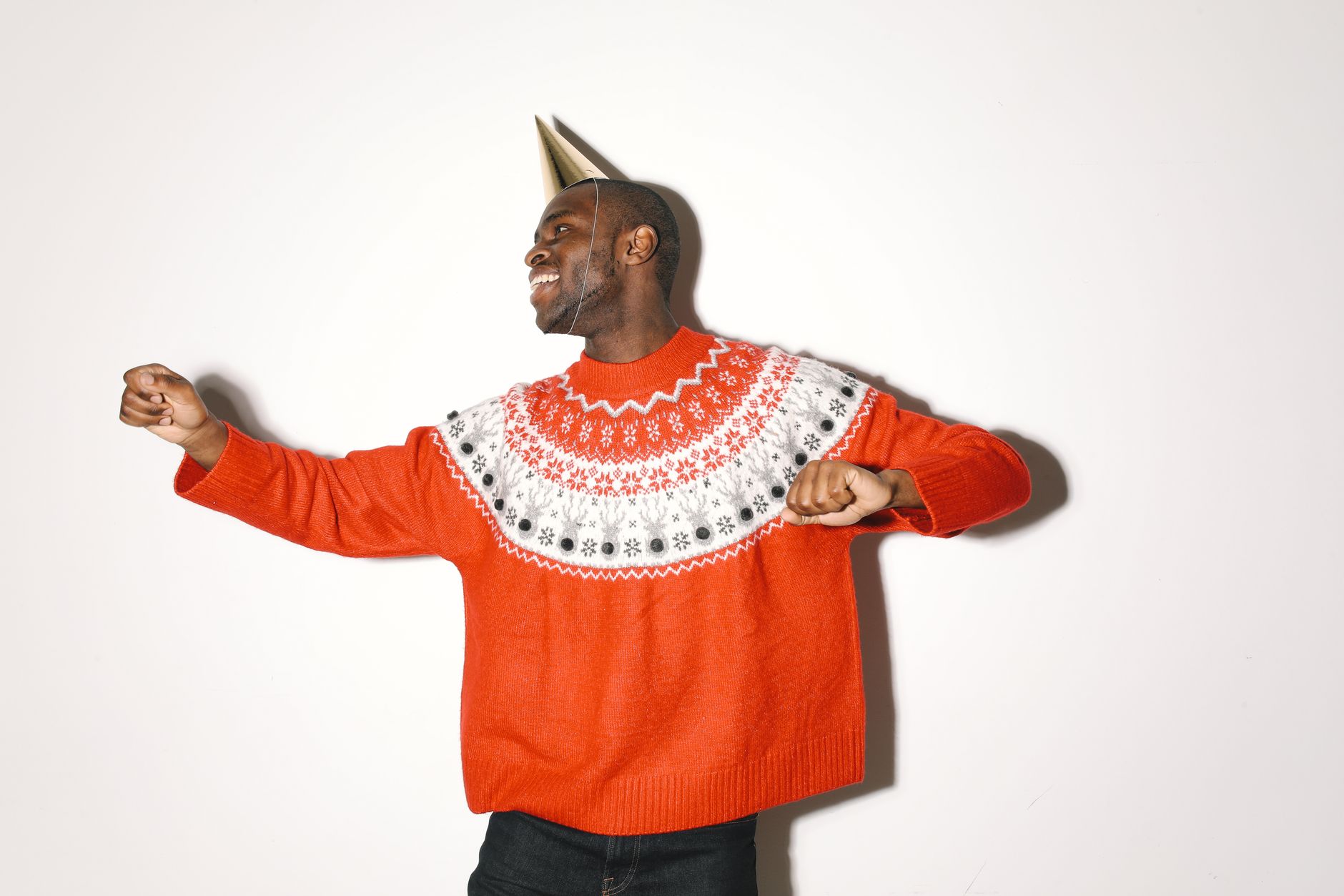 Joyful African American man in a festive sweater and party hat dancing happily.
