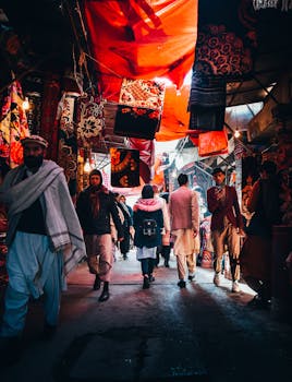 An illuminated alley market with diverse adults, showcasing colorful fabrics and bustling activity.