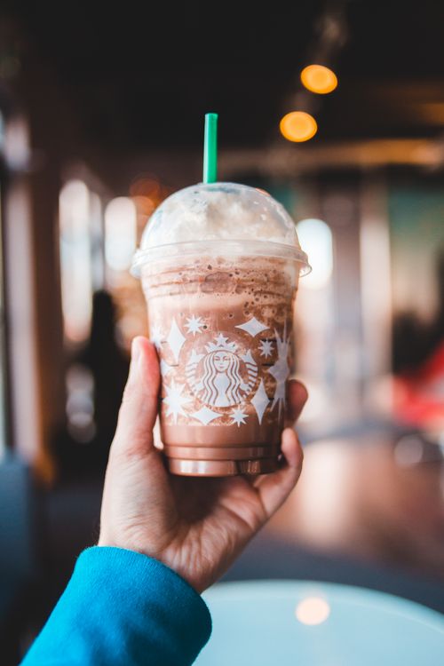 Free A refreshing iced coffee beverage in a disposable cup, held by a hand indoors. Stock Photo