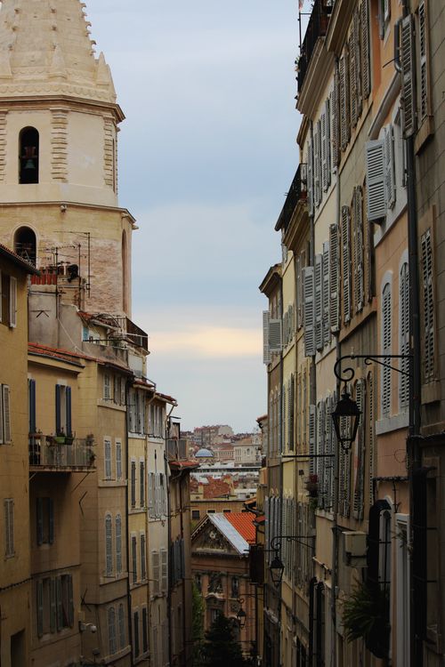 Free Discover a picturesque narrow street with charming old buildings and a historic tower in a cozy urban setting. Stock Photo