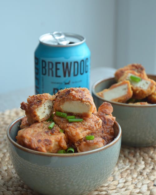 A Delicious Bowl of Fried Food Sprinkled with Scallions and a Beer in Can