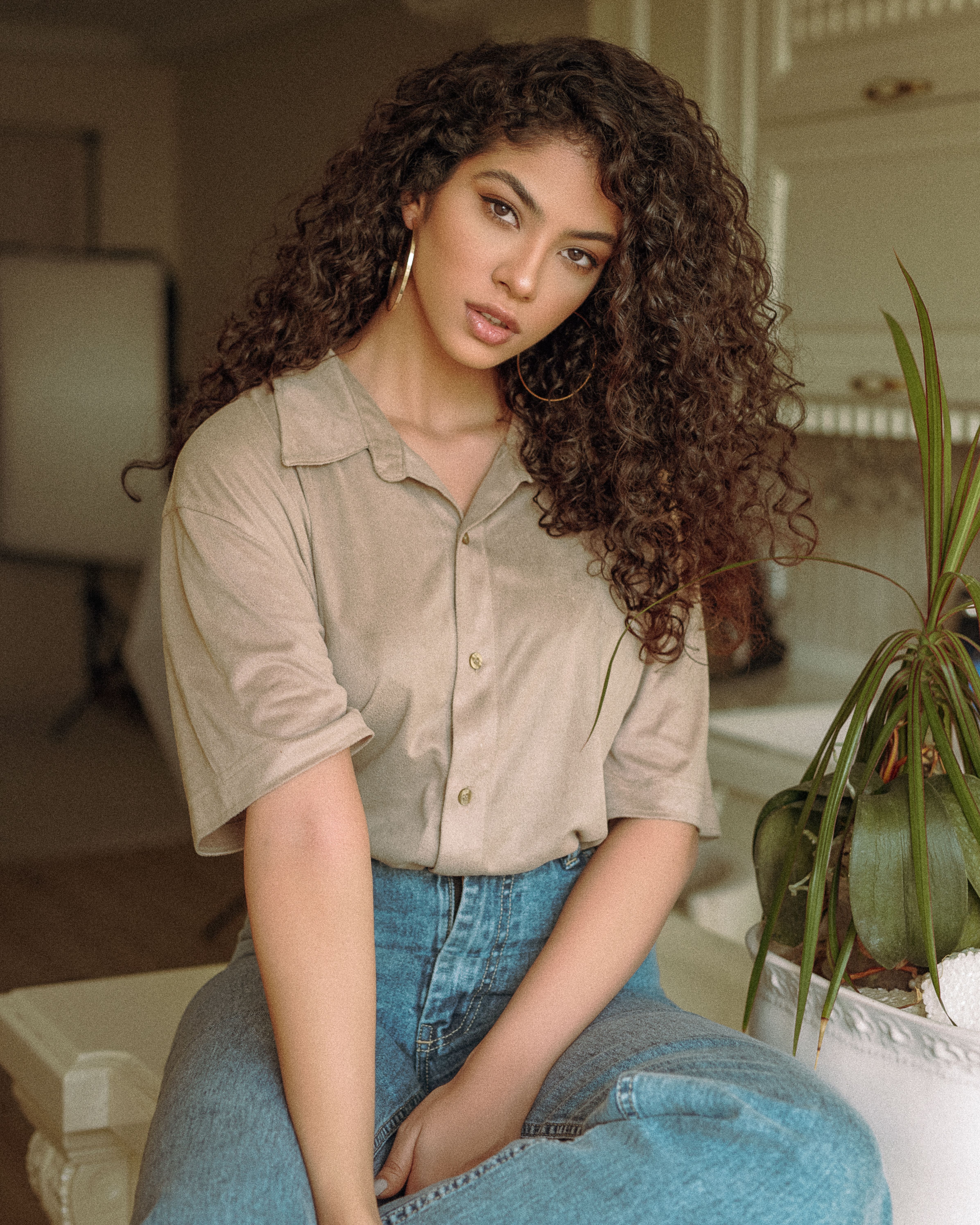 Elegant young woman with curly hair posing indoors, exuding fashionable charm.