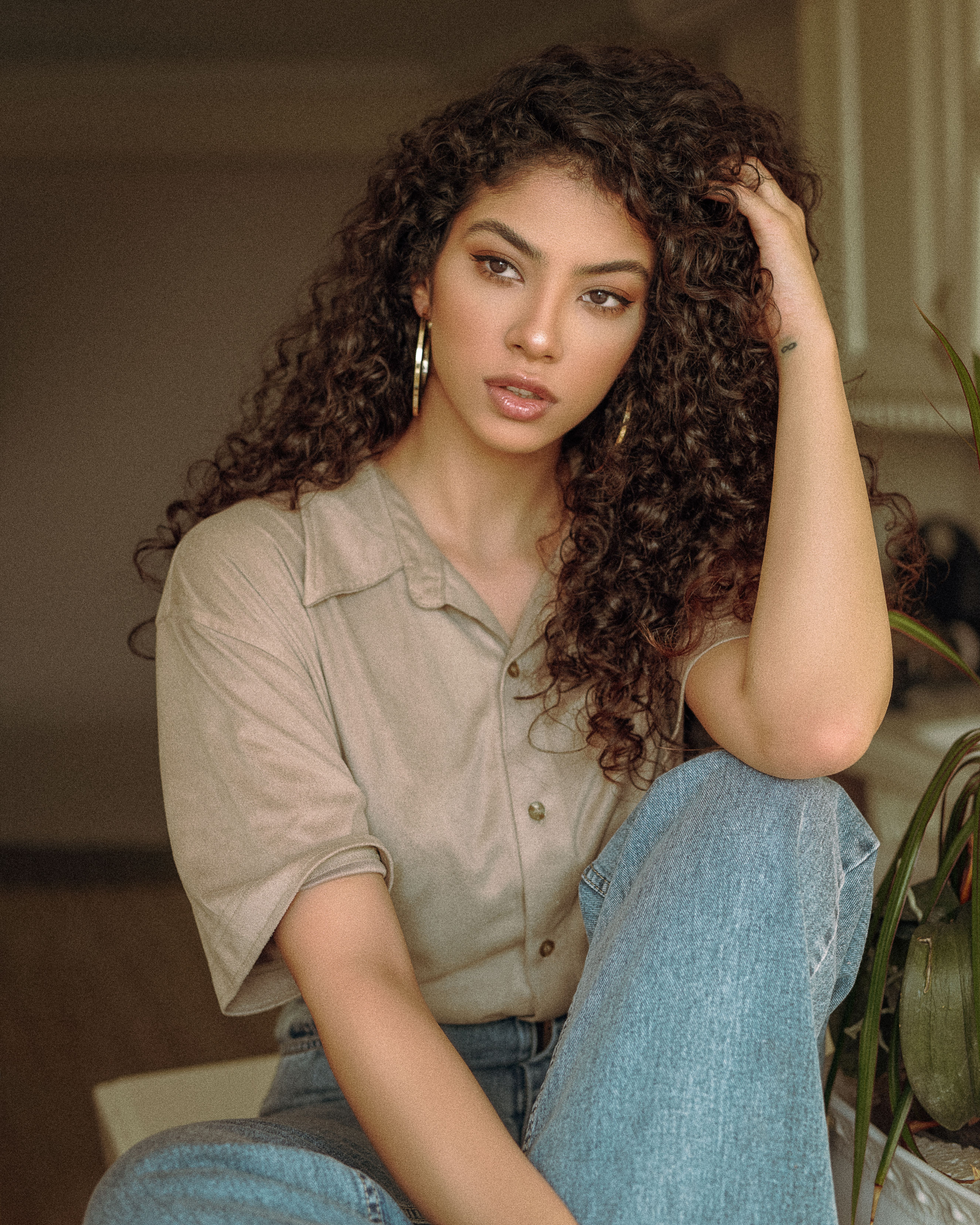 Elegant young woman posing indoors with curly hair and a relaxed expression.