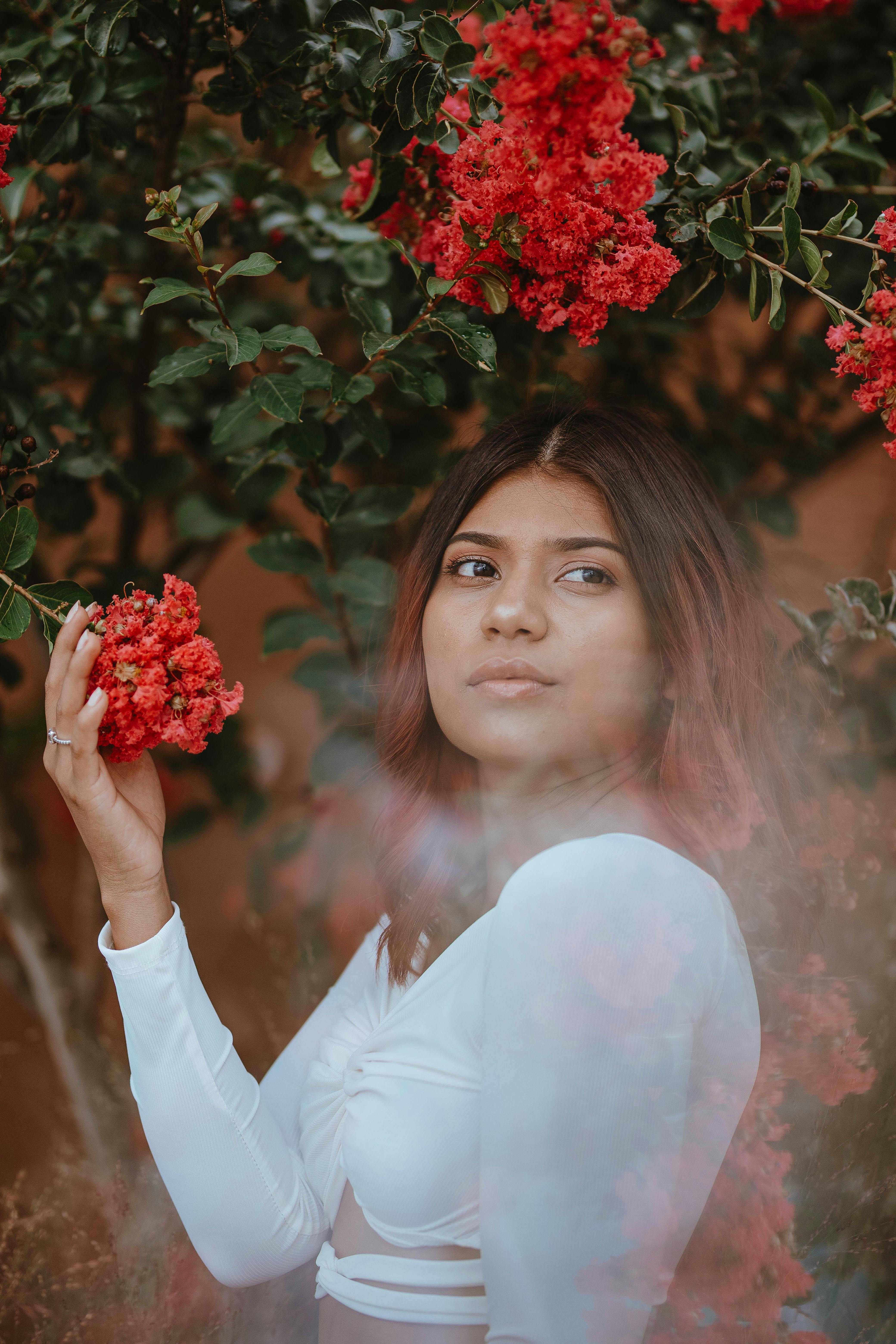 Stunning portrait of a woman posing with vivid red blossoms, creating a serene and artistic ambiance.
