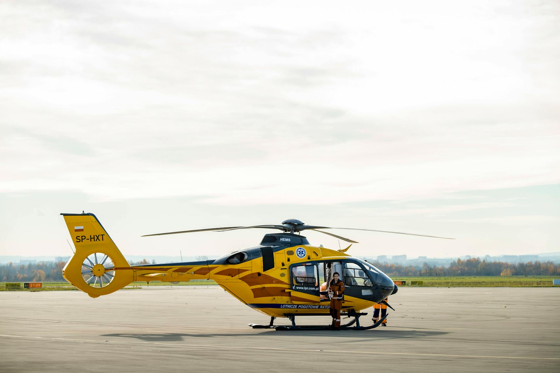 Yellow air ambulance helicopter on airfield with personnel in Poland, clear sky.