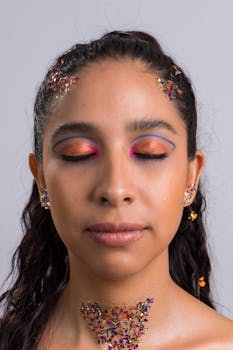 Close-up portrait of a woman with colorful makeup and glitter accents, eyes closed.