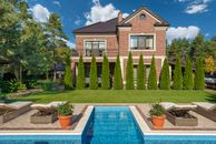 Facade of brick dwell villa with green bushes on lawn and sunbeds near swimming pool
