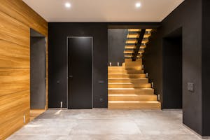 Interior of empty hallway with dark door in wall and stylish wooden stairs