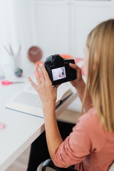 A woman examines photos on a DSLR camera while seated at a desk indoors.