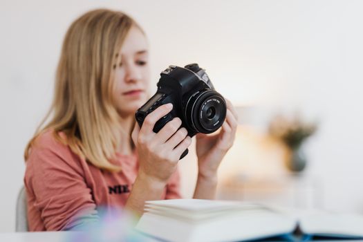 Young woman examining a DSLR camera indoors with a blurred background.