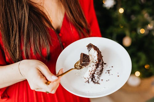 Free Woman in Red Long Sleeve Shirt Holding White Ceramic Plate With Chocolate Cake Stock Photo