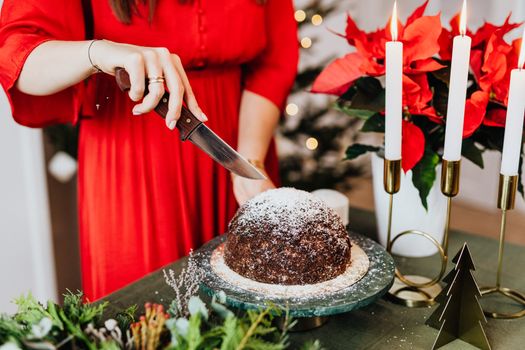 Woman slicing chocolate cake with festive decorations for Christmas celebration indoors.