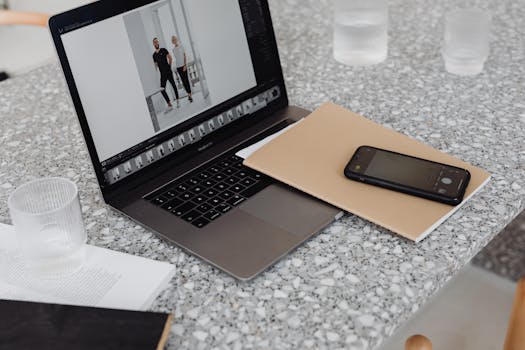 Modern workspace with a laptop, notebook, and smartphone on a terrazzo table surface.