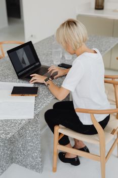 Blonde woman typing on a laptop at a modern granite desk in a minimalist office setting.