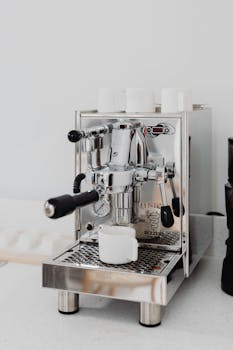 Close-up of a stainless steel espresso machine and cup in a modern kitchen setting.