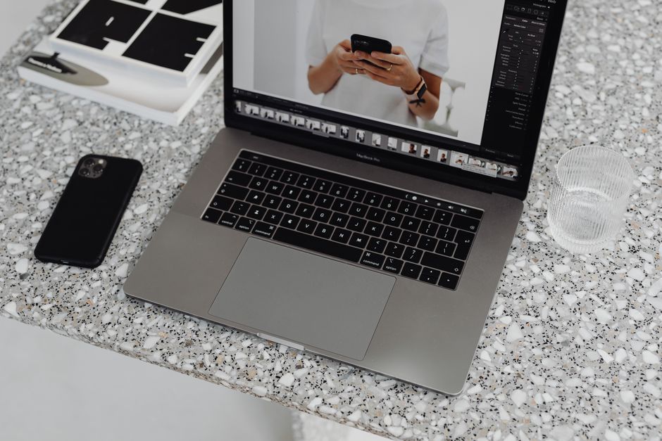 A sleek laptop and smartphone on a stylish marble surface with a glass of water nearby.