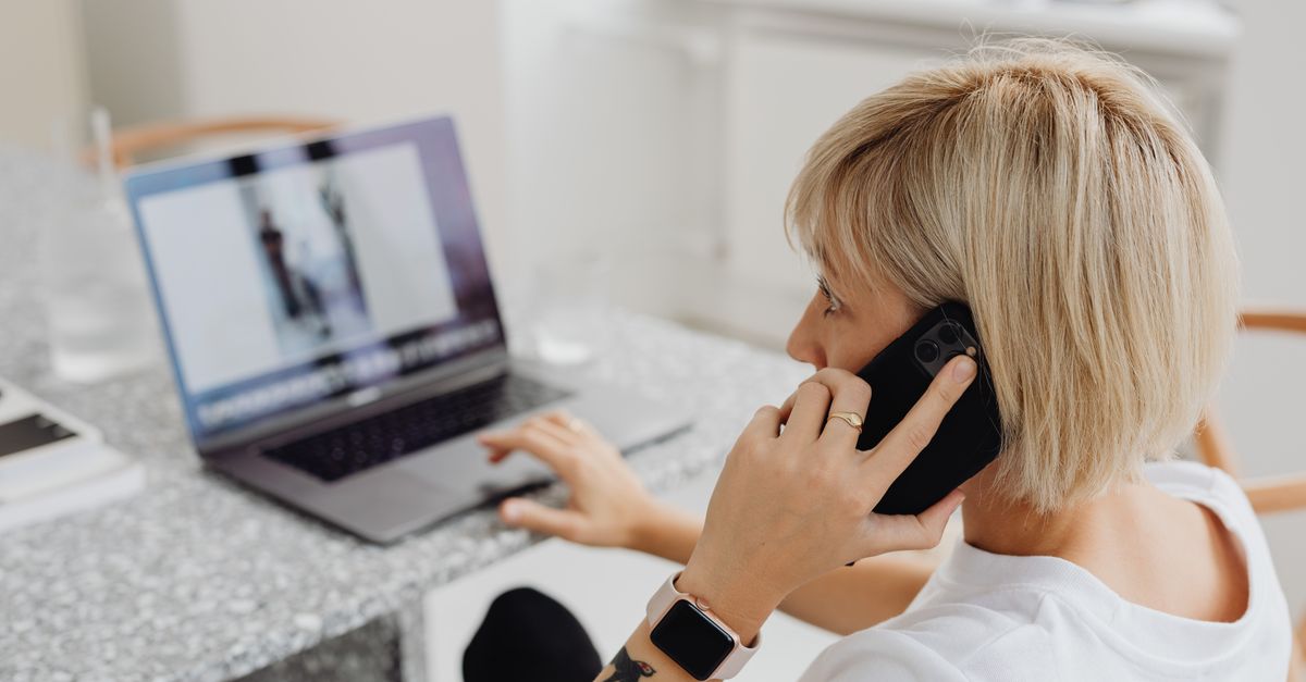 person pointing at a laptop screen while talking on the phone