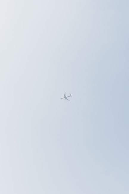 From below of modern passenger aircraft flying high in cloudless sky over ground