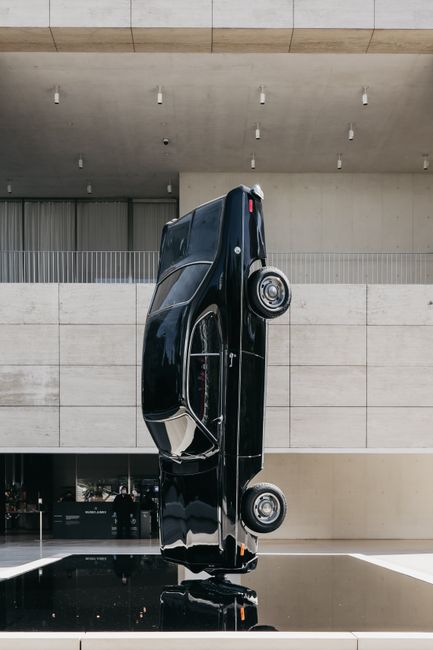 Upturned modern black automobile placed on platform as exhibit item in contemporary museum