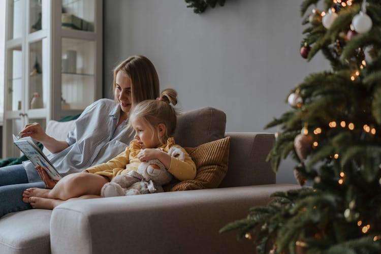 A Woman And A Child Reading A Book On Sofa