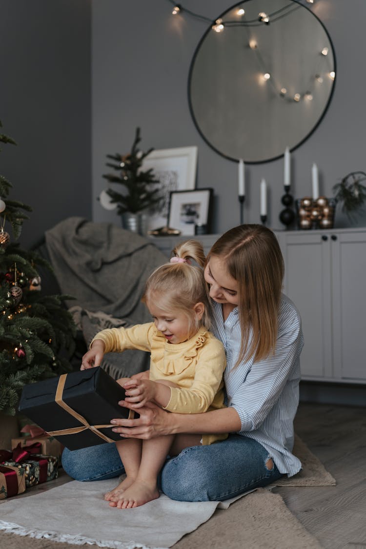 A Child Sitting On Mother's Lap Opening A Gift