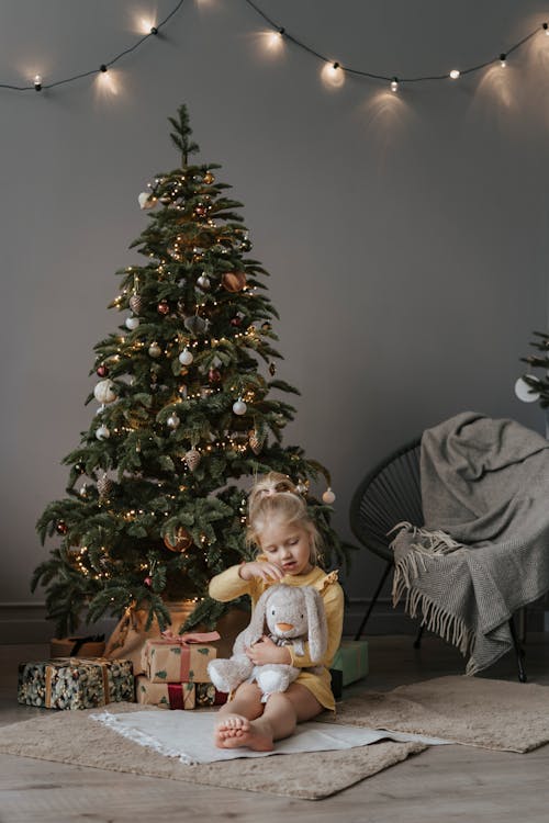 Girl in Yellow Long Sleeve Dress Sitting beside Green Christmas Tree