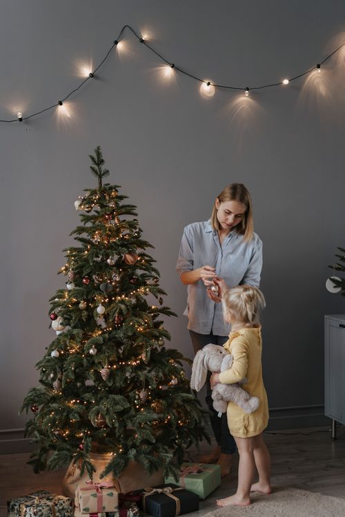 Free A mother and daughter decorate a Christmas tree with ornaments and lights indoors. Stock Photo