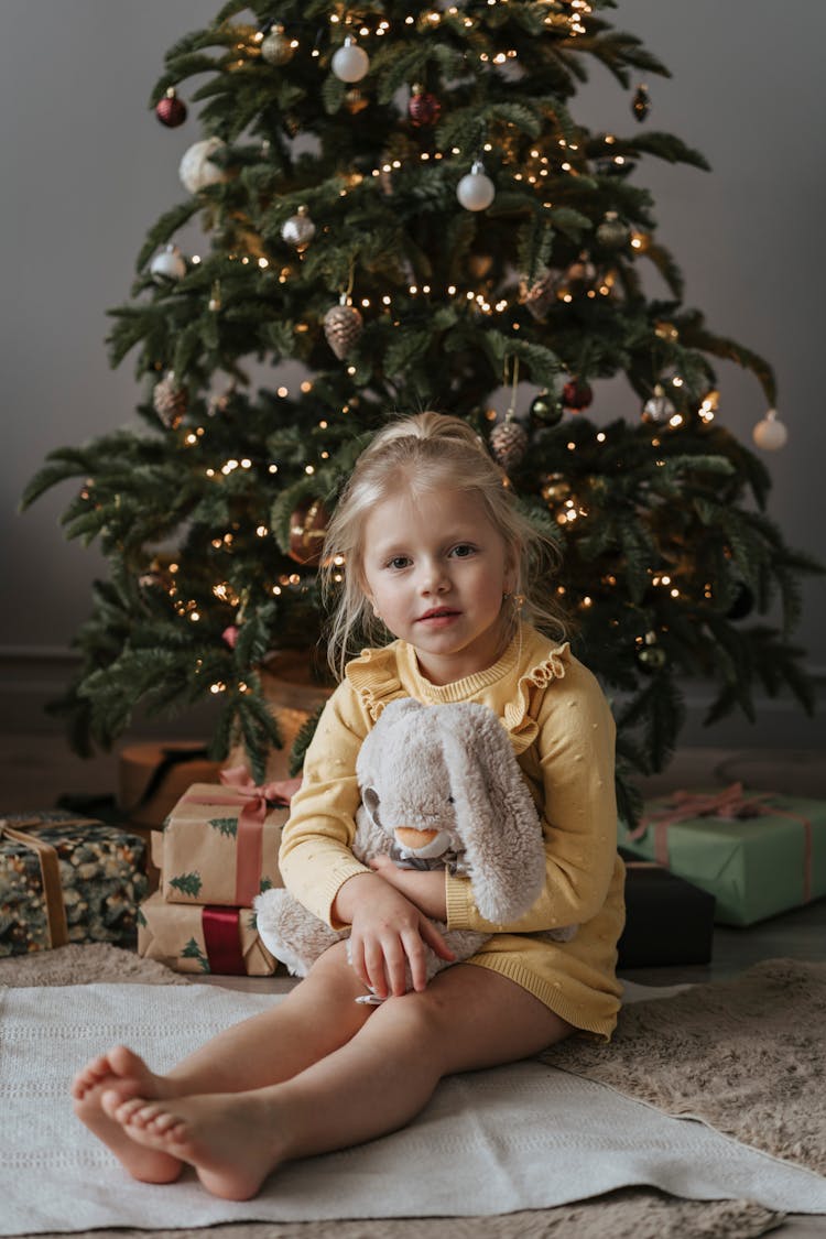 An Adorable Girl Sitting On Rug Holding A Plush Toy