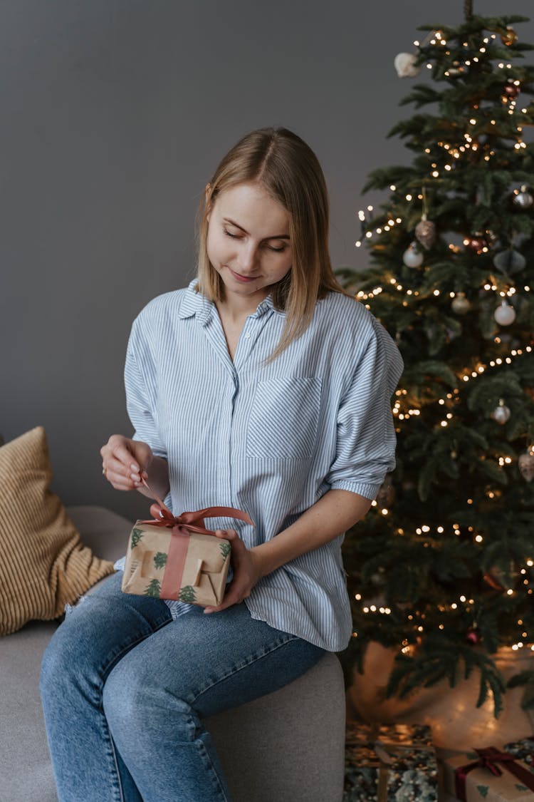 A Woman Opening A Gift Beside A Christmas Tree 