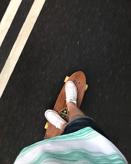 A Person Wearing White Sneakers Riding a Brown Skateboard
