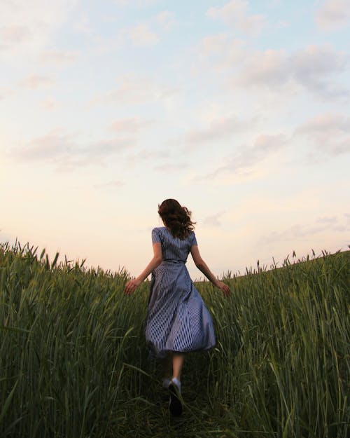 Woman in Blue Striped Dress Running on the  Green Grass Field