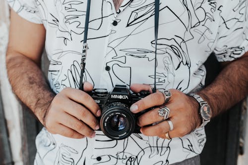 Crop anonymous male photographer in casual wear with accessories standing with professional photo camera