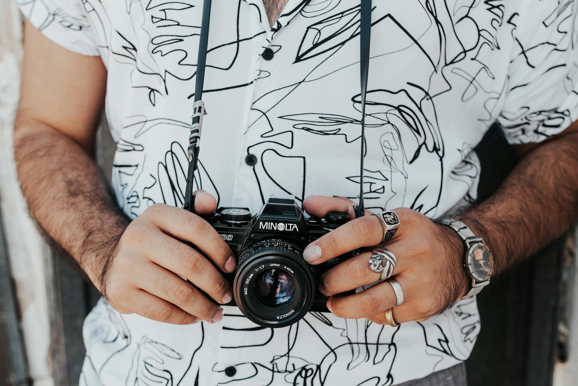 Crop anonymous male photographer in casual wear with accessories standing with professional photo camera