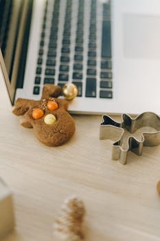 A gingerbread cookie and cookie cutter beside a laptop on a wooden surface.