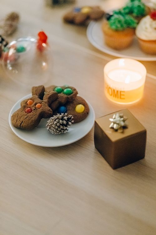 Free Delicious Christmas cookies on a plate with a lit candle and gift box, creating a festive atmosphere. Stock Photo