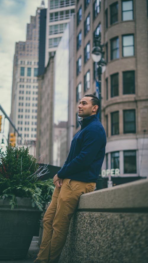 Side view of pensive African American male leaning on barrier while standing on street with modern residential buildings in city