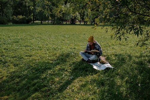 A Man Sitting on Grass Field while Reading a Book for Information