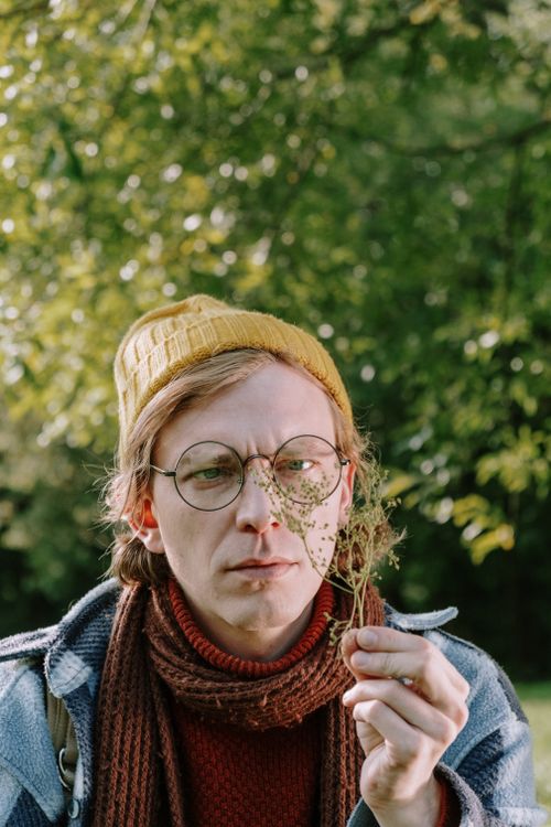 Free A man wearing glasses and a hat examining a plant in a lush green park. Stock Photo