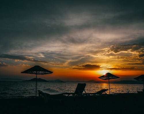 Silhouette De Deux Personnes Assises Sur Une Chaise Près De La Plage Pendant Le Coucher Du Soleil