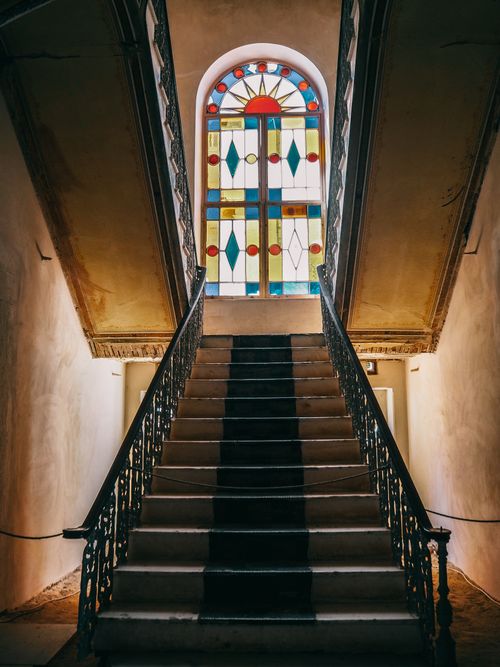 Free Elegant staircase with intricate railings leading up to a colorful stained glass window. Captured indoors. Stock Photo