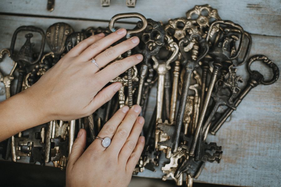 Close-up view of hands with rings holding an array of vintage skeleton keys on a wooden surface.
