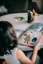 Back view of unrecognizable little girl sitting at table and turning pages of book with pictures