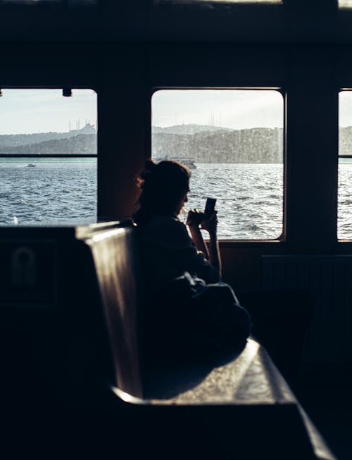 Женщина в черном пиджаке сидит на окне и смотрит на море