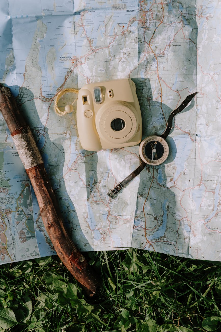 Flat lay of vintage camera, compass, and walking stick on a map outdoors.