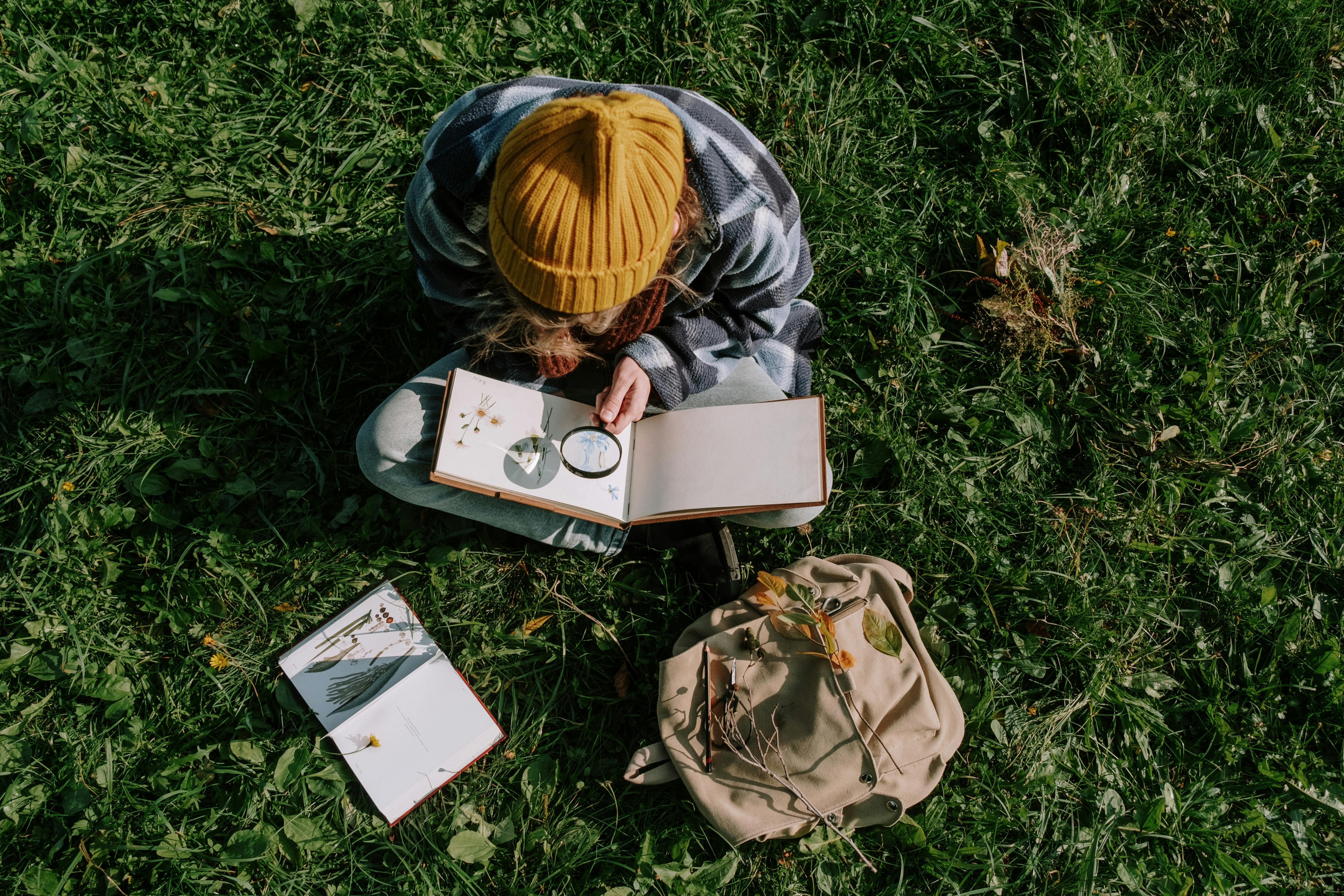 man in brown and black jacket reading book on green grass field