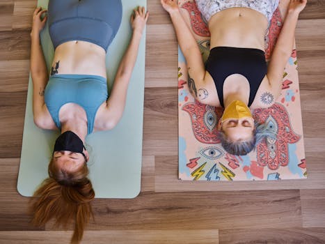 Two women meditating with face masks on colorful yoga mats indoors.
